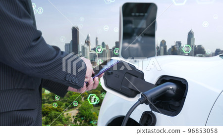 Progressive businessman recharge his EV car in esg city with ecological symbols. 96853058