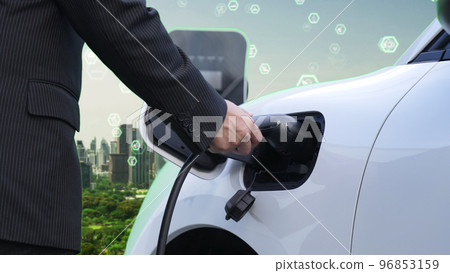 Progressive businessman recharge his EV car in esg city with ecological symbols. 96853159