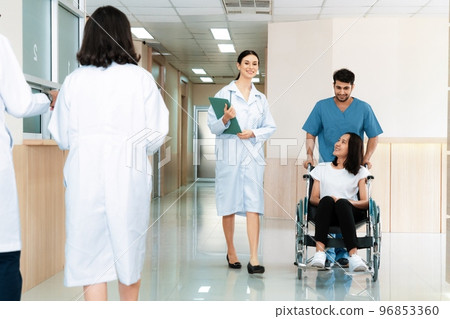 Doctor and nurse transport female patient in wheelchair at sterile corridor. 96853360