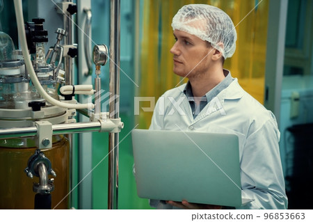 Apothecary scientist working with laptop near CBD oil extractor in laboratory. 96853663