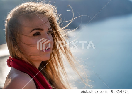 A woman in a red flying dress fluttering in the wind, against the backdrop of the sea. A woman in a red flying dress fluttering in the wind, against the backdrop of the sea. 96854774