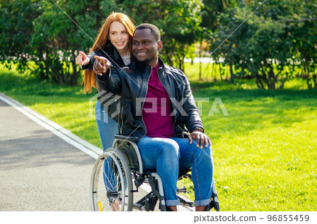 travel insurance concept.international couple in love in park next to wheel chair.finger pointing at something interesting into the distance travel insurance concept.international couple in love in park next to wheel chair.finger pointing at something interesting into the distance 96855459