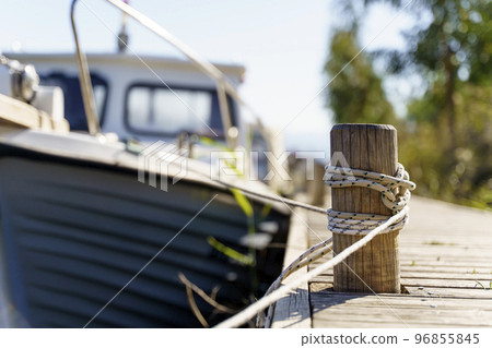Yacht on a rope at the pier. Sea vessel is moored to an old wooden pier on a sunny summer day. 96855845