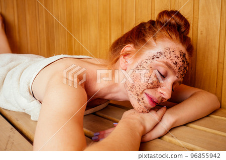 redhaired ginger young woman peeling face with brown sugar in traditional russian banya.steaming and self-care in finnish sauna 96855942