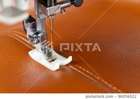 Modern sewing machine presser foot with a needle sews brown leather Modern sewing machine presser foot with a needle sews brown leather 96856022