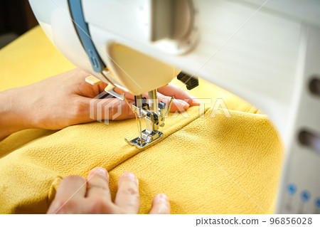 Female hands stitching yellow fabric on modern sewing machine. Close up view of sewing process. Female hands stitching yellow fabric on modern sewing machine. Close up view of sewing process. 96856028