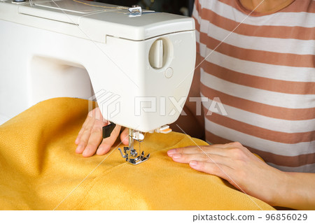 Female hands stitching yellow fabric on modern sewing machine. Close up view of sewing process. Female hands stitching yellow fabric on modern sewing machine. Close up view of sewing process. 96856029