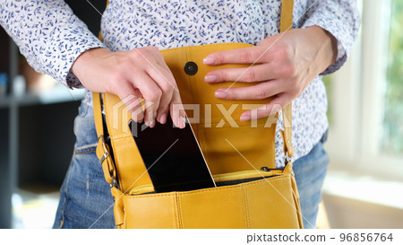 Woman in casual clothes put her smartphone in bright yellow shoulder bag. 96856764