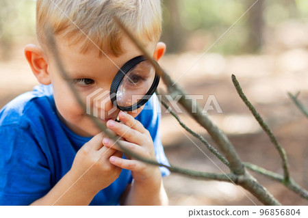 Curious boy is exploring nature with magnifying glass outdoors 96856804