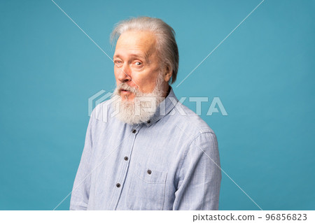 Portrait of white bearded candid old man wink wear good look clothing isolated over blue color background - positive human emotions face expression feelings Portrait of white bearded candid old man wink wear good look clothing isolated over blue color background - positive human emotions face expression feelings 96856823