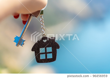 Keys with a keychain in the shape of a house in a female hand against the backdrop of the sea. The concept of buying a house, apartment, real estate, young family, mortgage loan, rental housing. 96856959
