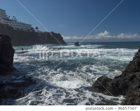 View of natural rock swimming pool Charco de Isla Cangrejo in the Atlantic Ocean in Los Gigantes, Tenerife, Canary islands, Spain. Sunny winter day. View of natural rock swimming pool Charco de Isla Cangrejo in the Atlantic Ocean in Los Gigantes, Tenerife, Canary islands, Spain. Sunny winter day. 96857307