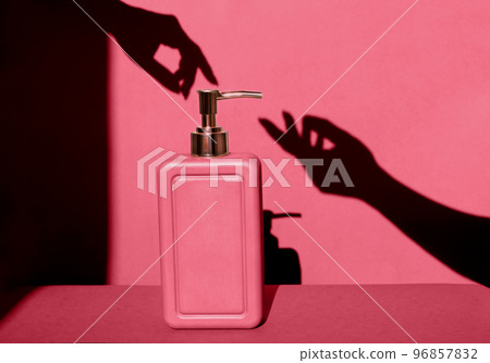 Cosmetic product in stylish red marble bottle with dispenser and shadow of elegant female hands on viva magenta studio background. Hand skin care with moisturizer and natural soap. 96857832