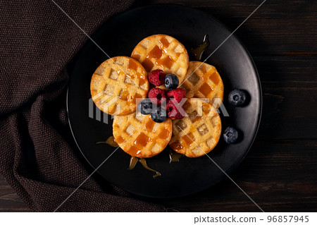 Small round waffles with berries on dark background, flat lay Small round waffles with berries on dark background, flat lay 96857945