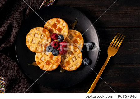 Small round waffles with berries on dark background, flat lay Small round waffles with berries on dark background, flat lay 96857946