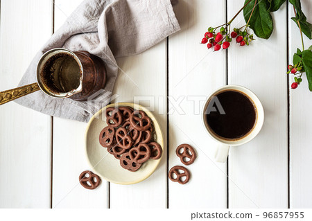 Top view of a cup of coffee, coffee pot and chocolate-covered pretzels 96857955