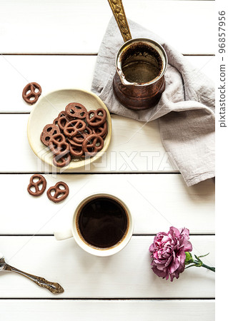 A cup of coffee, empty coffee pot, chocolate-covered pretzels and a flower A cup of coffee, empty coffee pot, chocolate-covered pretzels and a flower 96857956
