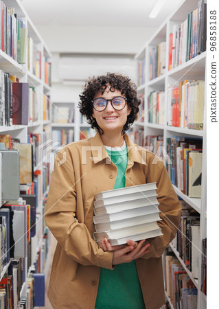 young woman with curly hair in library among shelves with books. female student conducts scientific work young woman with curly hair in library among shelves with books. female student conducts scientific work 96858188