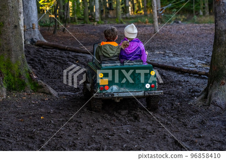 Children ride in an open iron children's car. Extreme form of entertainment for children. The boy drives through the mud, accompanied by his sister  96858410