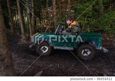 A Teen ride in an open iron children's car. Extreme form of entertainment for children. The boy drives through the mud in the forest A Teen ride in an open iron children's car. Extreme form of entertainment for children. The boy drives through the mud in the forest 96858412