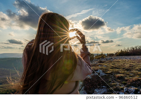 The girl made a beautiful heart from her finger in the rays of the sun. healthy woman making heart shape with hands at sunset. Shining summer sun on your hands. healthy heart concept. 96860512