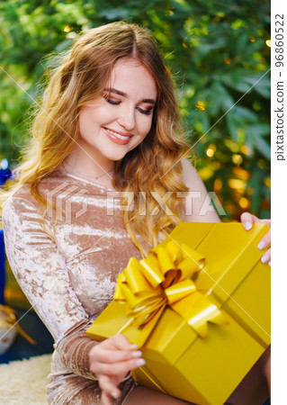 a beautiful woman in a shiny dress with a gift by the christmas tree. a beautiful woman in a shiny dress with a gift by the christmas tree. 96860522