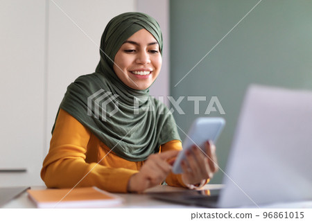 Muslim Woman Shopping Online With Smartphone While Sitting At Desk In Office 96861015