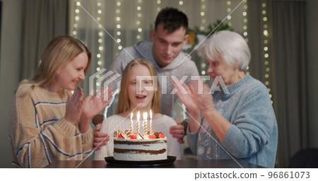 A teenage girl blows out the candles on her birthday cake. Near her relatives clapping for her A teenage girl blows out the candles on her birthday cake. Near her relatives clapping for her 96861073