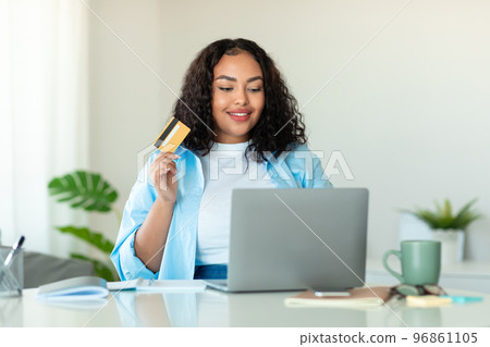 Young black oversize woman with credit card using laptop at home, ordering food or shopping online, copy space 96861105