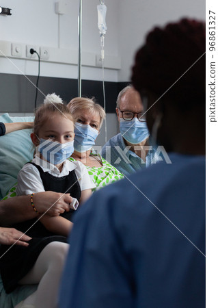 Little girl talking to female nurse. Elderly couple, granddaughter listening recommendations to avoid covid 19 infection. African american geriatrician caring elderly woman. 96861327