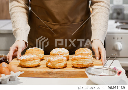 Woman prepares fresh donuts with jam in home kitchen. Cooking traditional Jewish Hanukkah sufganiyot. 96861489