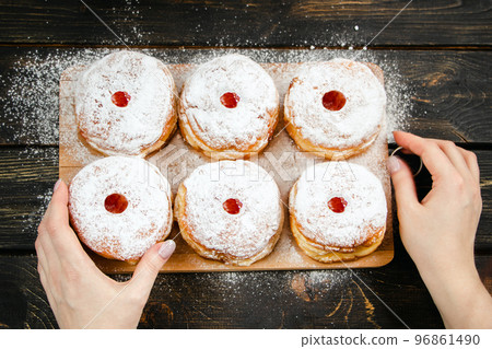 Cooking traditional Hanukkah sufganiyot. Woman sprinkles donuts with powdered sugar. 96861490
