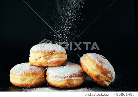 Powdered sugar is poured onto donuts. Traditional Jewish dessert Sufganiyot on black background. Cooking fried Berliners. 96861493