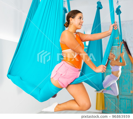 Girl doing unicorn pose in hanging hammock during aerial yoga group training 96863939