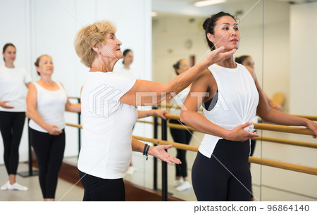 Elderly ballet instructor adjusting students form 96864140