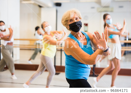 Active mature woman in a protective mask practices energetic swing in the studio 96864171