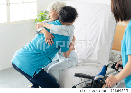 A caregiver transferring an elderly person from a nursing bed to a wheelchair A caregiver transferring an elderly person from a nursing bed to a wheelchair 96864855