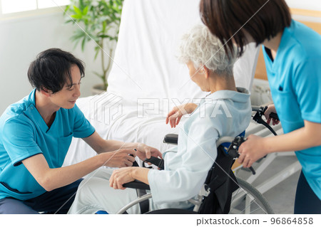 A caregiver transferring an elderly person from a nursing bed to a wheelchair 96864858
