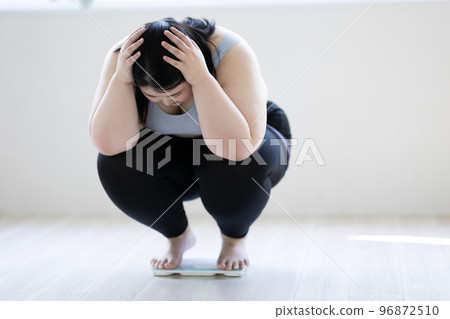 A woman holding her head on a weight scale 96872510