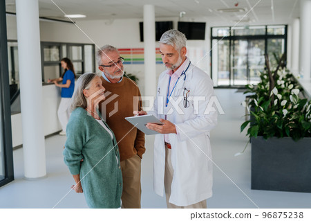 Mature doctor talking with his senior patients at hospital corridor. 96875238