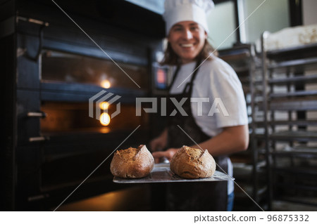 Happy young baker with fresh bread, in bakery. 96875332