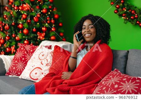 Young african woman talking on the smartphone sitting by christmas tree at home 96876912