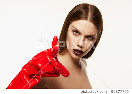Portrait of beautiful young woman with straight brown hair and dark makeup posing in red rubber gloves over white background. Impressive look 96877765