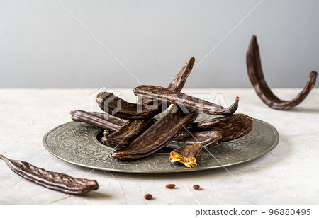 Carob pods group on grey antique plate with light grey background and copy space for text 96880495