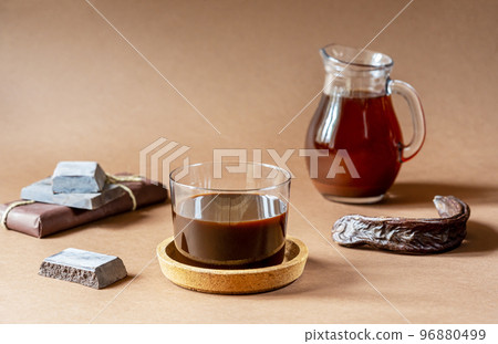 Carob molasses and beverage, chocolate and carob pods on light brown background and copy space for text Carob molasses and beverage, chocolate and carob pods on light brown background and copy space for text 96880499