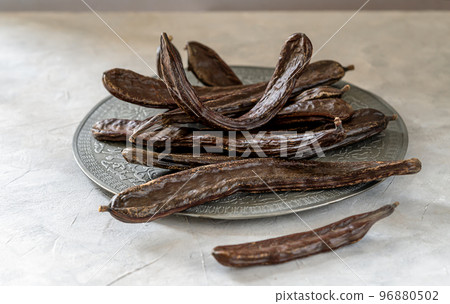 Carob pods group on grey antique plate with light grey background Carob pods group on grey antique plate with light grey background 96880502