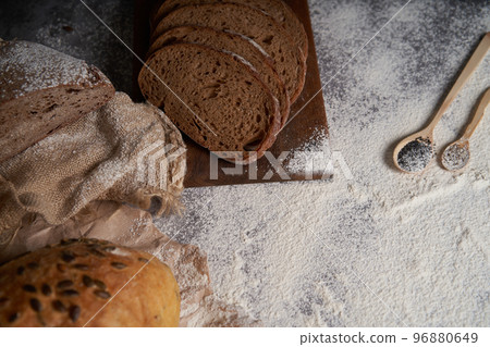 Top view of various types of bread, sliced and whole, flour, crumpled paper and burlap on a wooden table. High angle. Top view of various types of bread, sliced and whole, flour, crumpled paper and burlap on a wooden table. High angle. 96880649