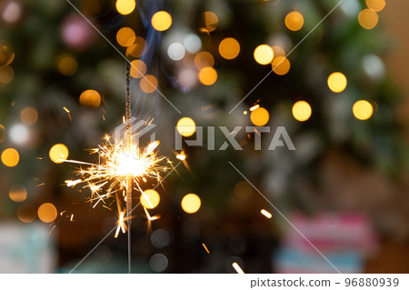 Christmas glittering sparklers candle burns in Christmas tree background. Xmas lighting decoration at home indoor. Festive Magic sparks lights for holiday party. Christmas eve with fireworks. Christmas glittering sparklers candle burns in Christmas tree background. Xmas lighting decoration at home indoor. Festive Magic sparks lights for holiday party. Christmas eve with fireworks. 96880939