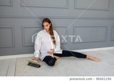 Long-haired cute pregnant woman sitting on the floor with a laptop 96881298