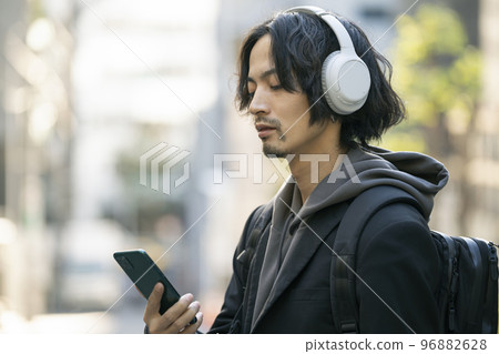Young man wearing headphones looking at smartphone screen Young man wearing headphones looking at smartphone screen 96882628